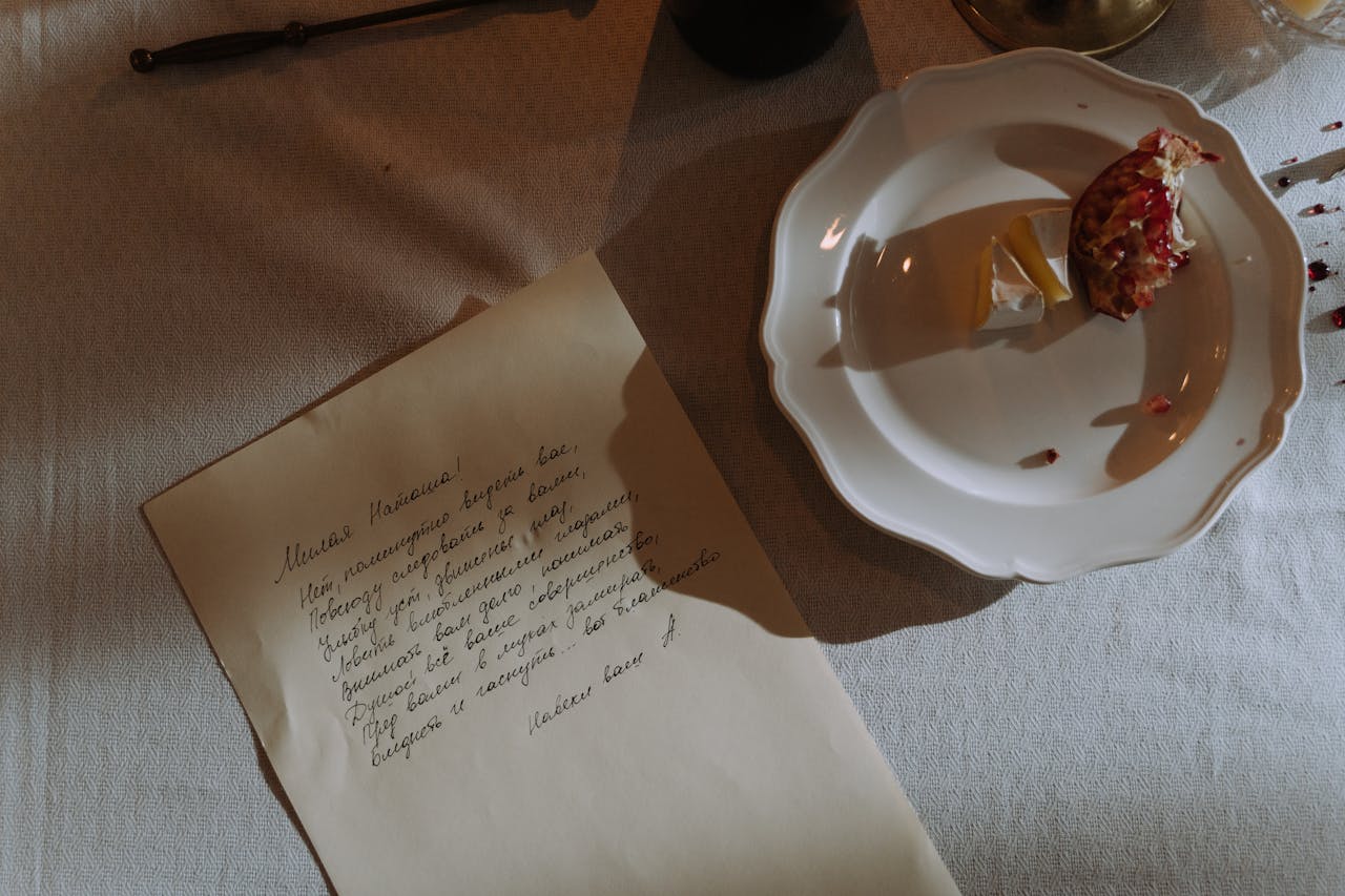 An artistic shot of a handwritten letter beside a plate of pomegranate and cheese on a textured fabric.